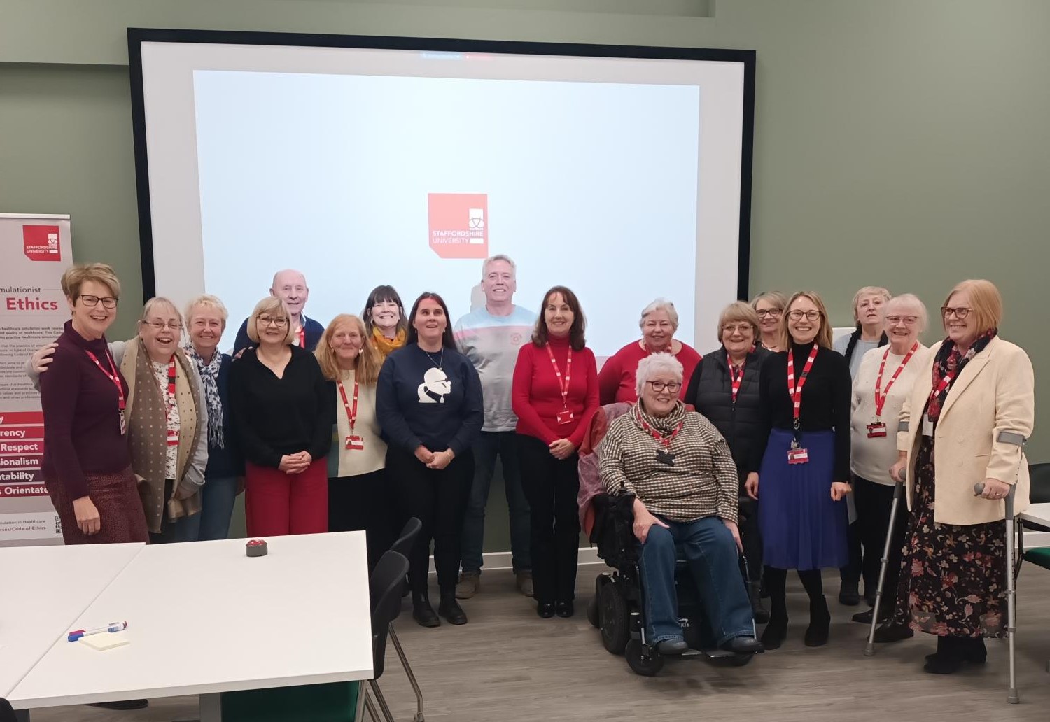 A group of diverse adults are smiling for a photo in a seminar room