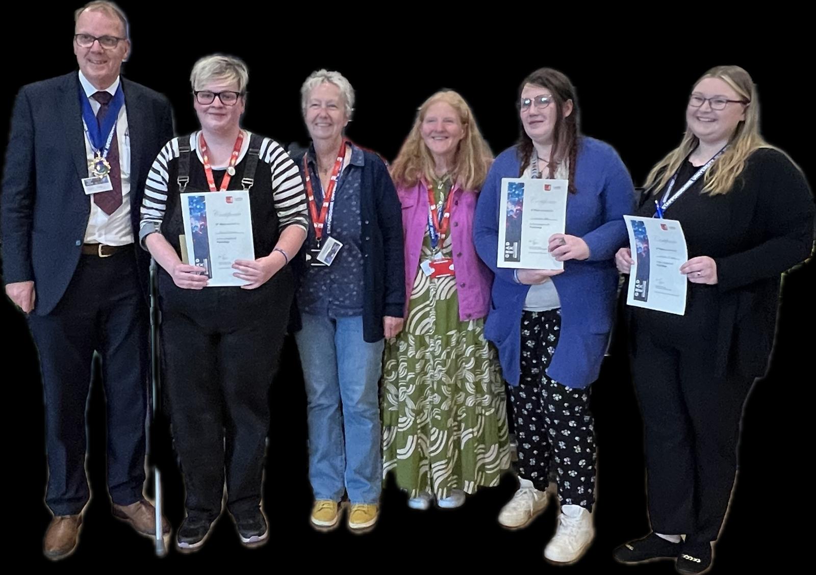 A group of students and community members are holding certificates of achievements smiling for a photo