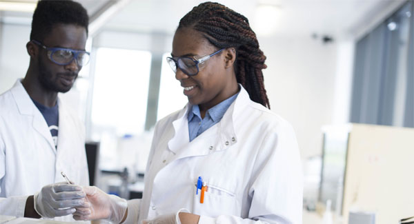 A male and female student wearing white lab coats working together with substances in the science lab