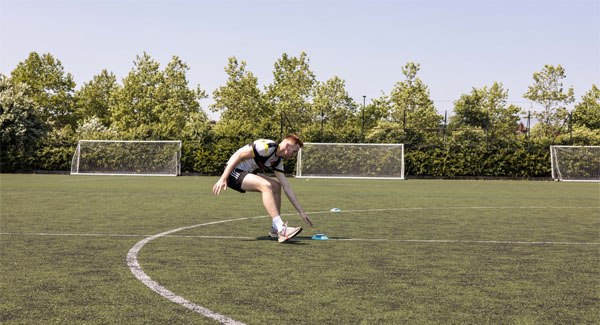 A male sports student wearing football kit is training on the outdoors university pitch