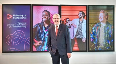 Suited man with hand in pocket stood in front of digital screens