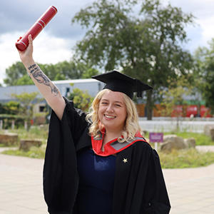 Charlotte Jacobs in her graduation cap and gown holding a scroll in the air