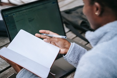 woman of colour sat with notebook in front of a laptop