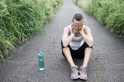 A runner pictured sitting on the ground next to a water bottle with their head in their hands