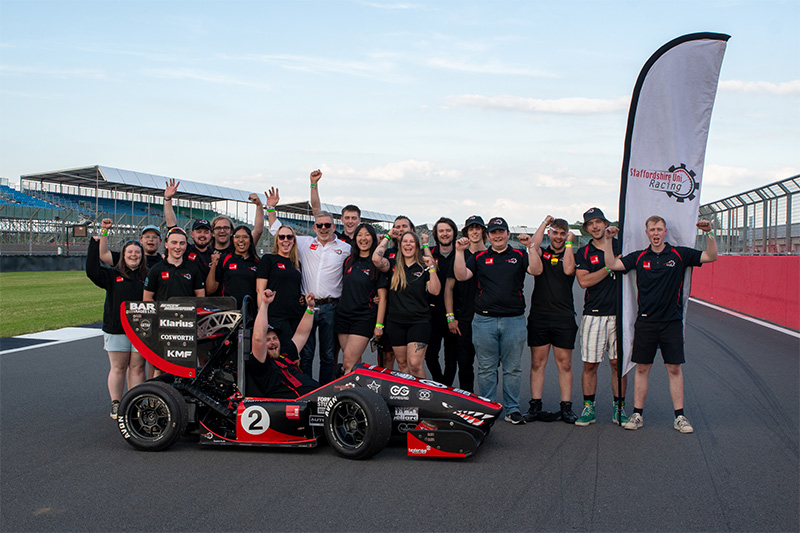 A group of Staffordshire University students on Silverstone racing track with the racing car they designed