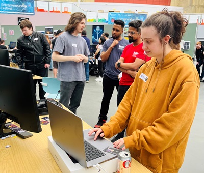 Girl on laptop computer and men stood around conversing