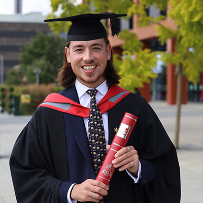 Harry Bamforth in his graduation cap and gown holding his scroll