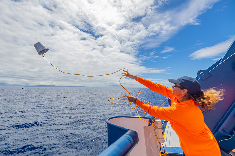 A person in an orange jumper throwing a bucket from a boat