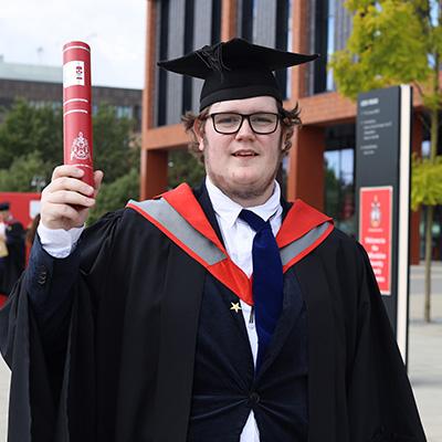 Joshua Lockley in his graduation cap and gown holding a scroll