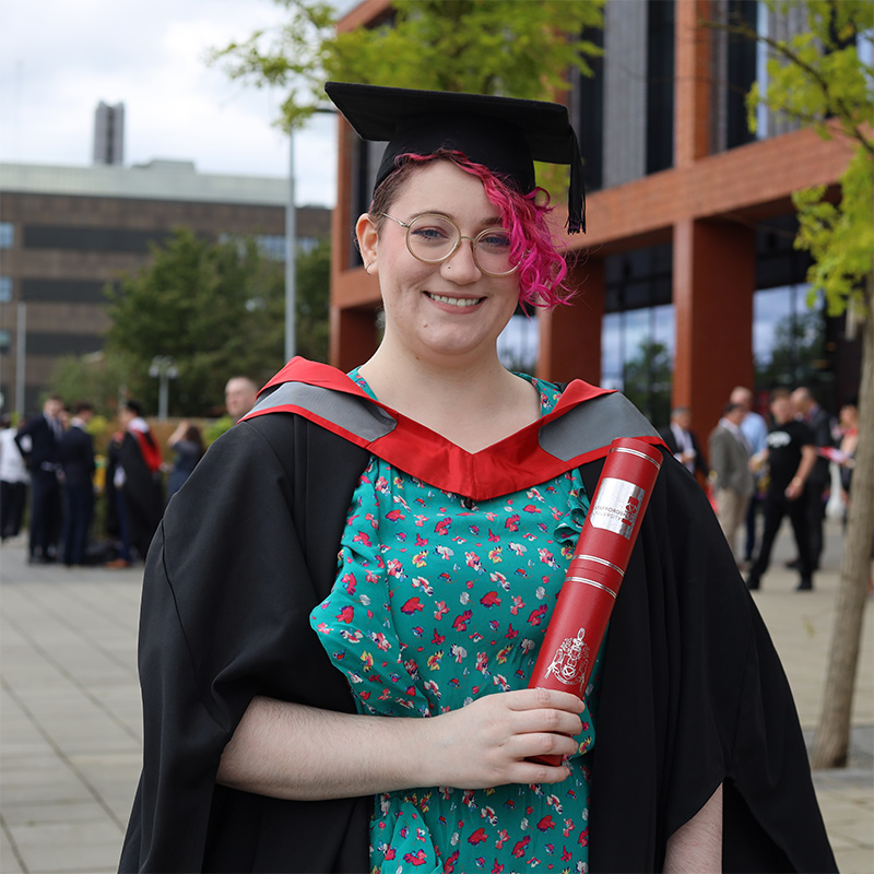 Opal Raine in their graduation cap and gown holding a scroll