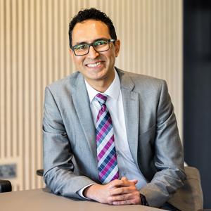 Smiling man in suit and wearing glasses seated at a desk