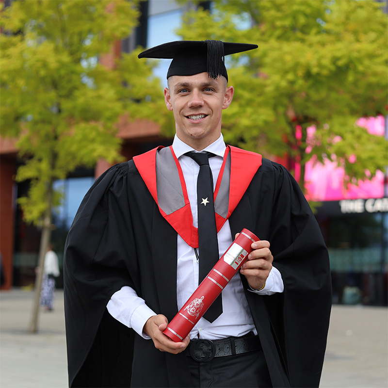 Sam Westley in his graduation cap and gown holding a scroll