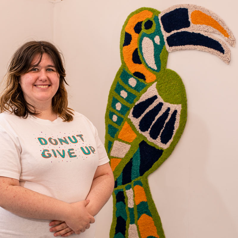 Student standing in front of their rug design in the Surface Pattern exhibit at the Art and Design Showcase