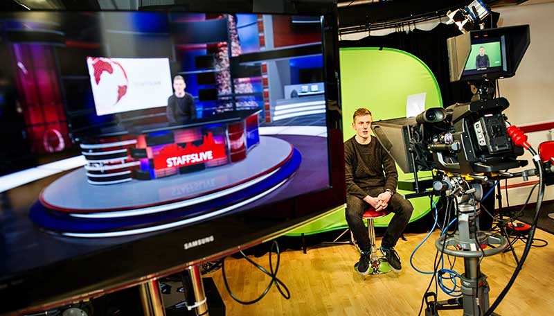 Male student sitting in front of a green screen