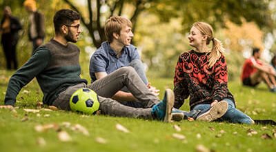 Three students sitting on the grass in the sun, enjoying life in the United Kingdom.