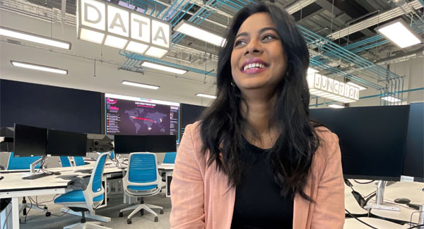 A female with dark long hair is sitting and smiling in the data pc lab