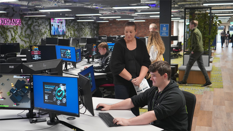 A young male is using a computer to test games in the modern computer suite