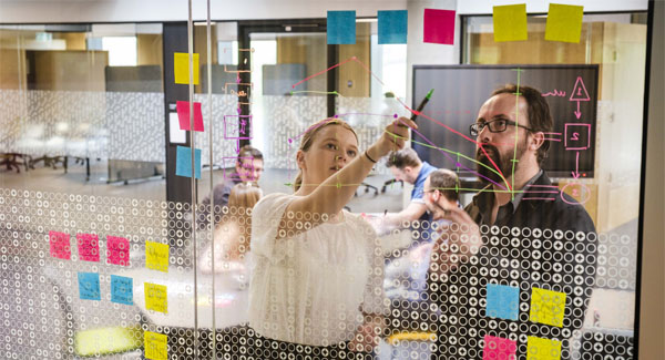 A team are collaborating on charts and notes on glass screen in an office environment