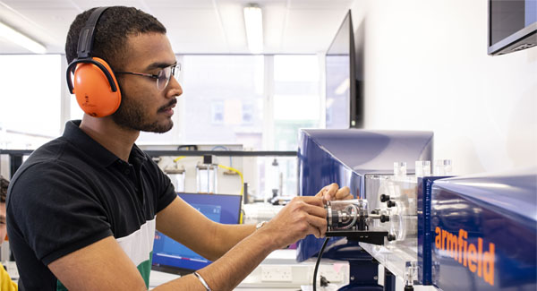 A male wearing casual clothes and protective ear wear is using engineering equipment at the University