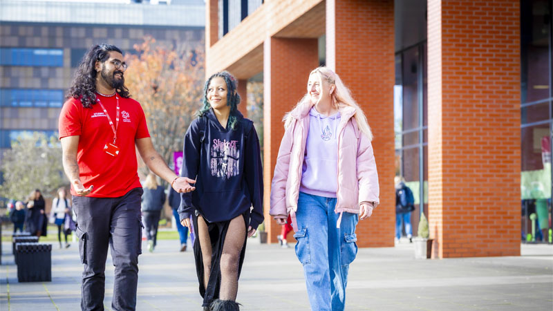 A student ambassador wearing a red tshirt is giving two female visitors a tour on Leek Road