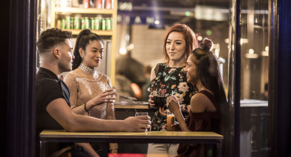 A group of students are in a modern bar area chatting with drinks in the evening