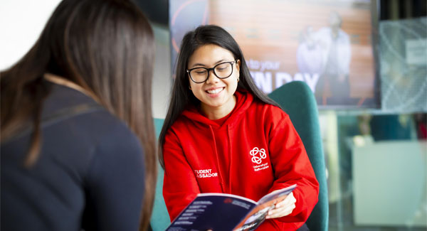 A female student ambassador wearing a red hoodie is sitting and giving university advice to a visitor