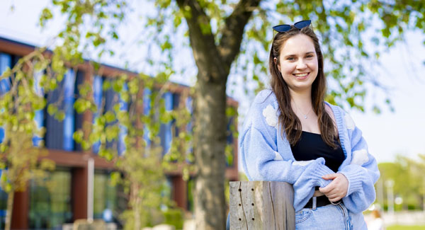 A female student wearing blue is standing on the green space outside the Catalyst